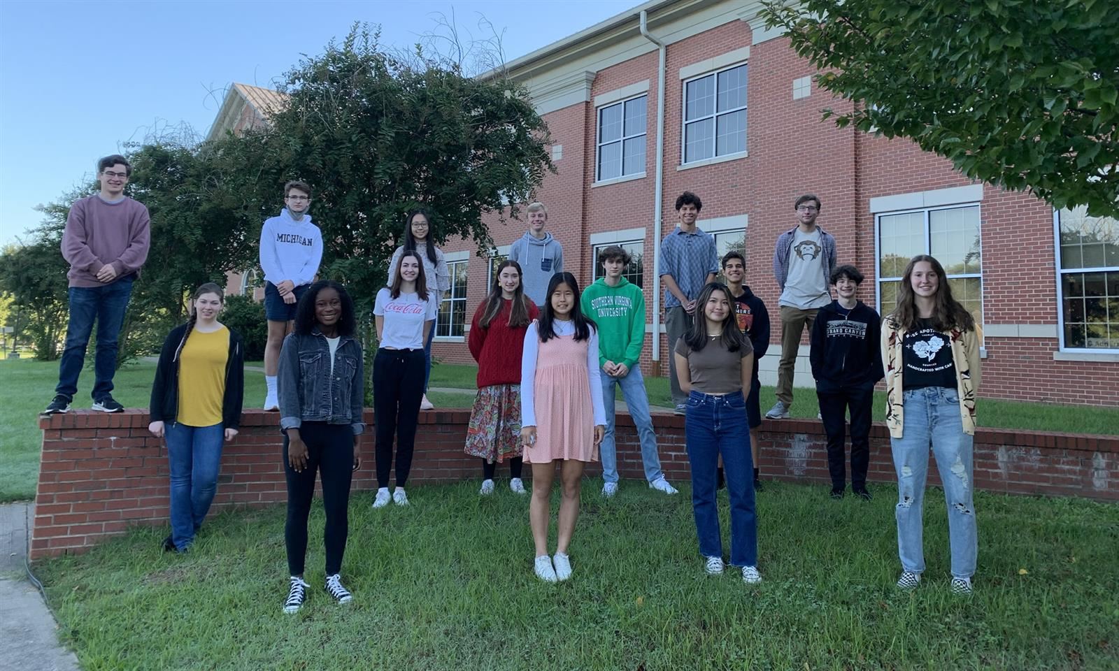 Students stand on a brick wall and in front of the school